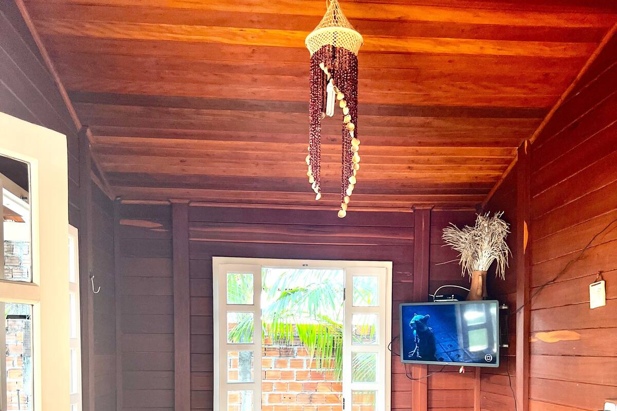 A wooden cabin room with two beds, a small table, a TV mounted on the wall, and a hanging light fixture.