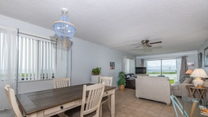 A dining area with a wooden table and chairs, a chandelier, and a view of the outdoors through large windows. - Maria Beautiful Beachfront Condo, sleeps up to 8. BIG DISCOUNTS NOW  (Flagler Beach)