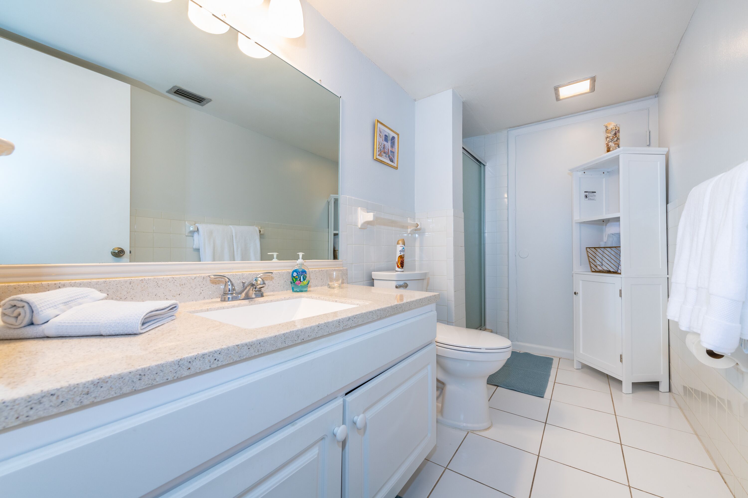 A bathroom with a white vanity, a sink, a toilet, and a mirror.