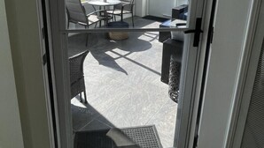 En glasdør fører ud til en patio med udendørs møbler, ventilator i loftet og udsigt over landskabet.