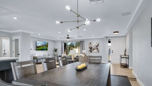 A modern dining area with a dark wooden table and chairs, a chandelier, and a large window providing natural light. - Minutes from Shopping, Dining & Golf (Scottsdale)