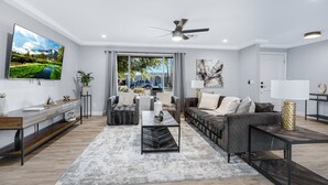 A modern living room with a flat-screen TV, a ceiling fan, and a large window. - Minutes from Shopping, Dining & Golf (Scottsdale)