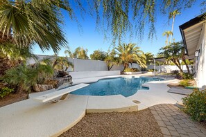 A swimming pool with a waterfall feature, surrounded by palm trees and a white wall. - Minutes from Shopping, Dining & Golf (Scottsdale)