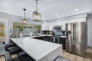 A modern kitchen with a large island, stainless steel appliances, and a hanging light fixture. - Minutes from Shopping, Dining & Golf (Scottsdale)