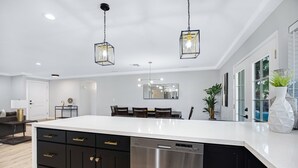 A modern kitchen with a large island, black cabinets, stainless steel dishwasher, pendant lighting, and a dining area with a table and chairs. - Minutes from Shopping, Dining & Golf (Scottsdale)