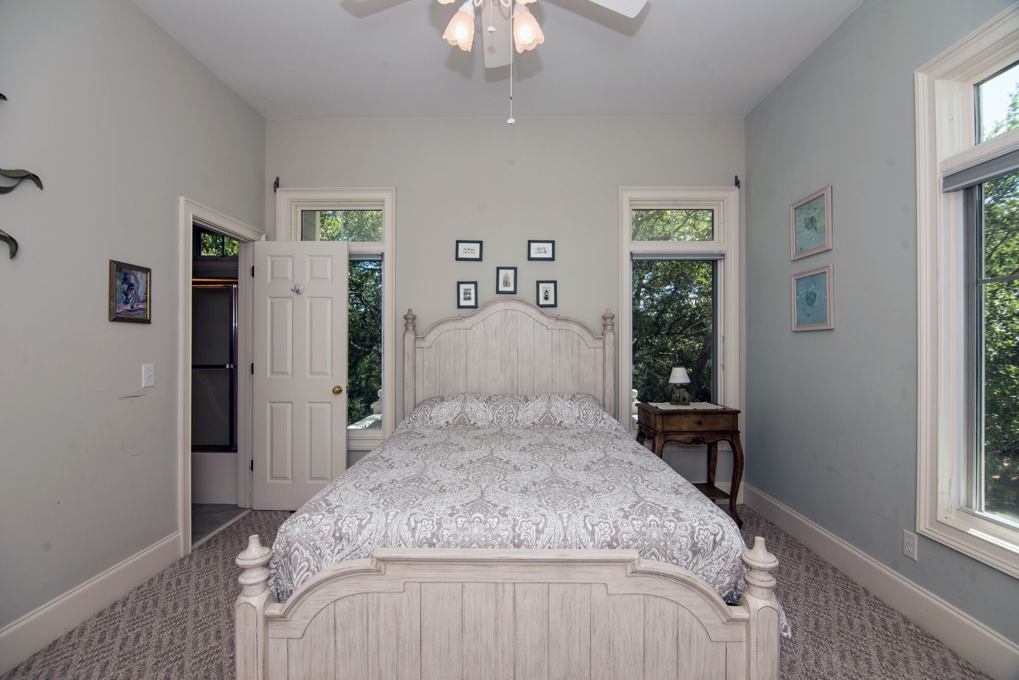 A bedroom with a large bed, two windows, and a door leading to another room.