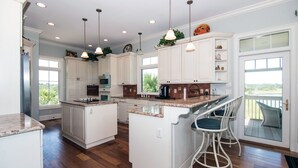A spacious kitchen with white cabinetry, a central island, bar stools, and a view to the outdoors.