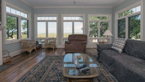 A spacious living room with large windows, a ceiling fan, and a view of the beach.