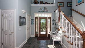A hallway with a wooden staircase, a bench, and a door leading to a glass door.