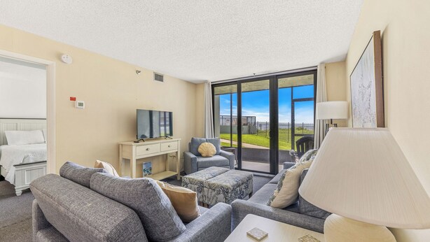 A modern hotel room with a large sliding glass door leading to a balcony, a sofa set, a small table, and a TV.