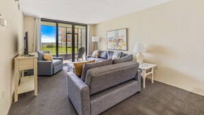 A modern living room with grey sofas, a small side table, a lamp, and a painting on the wall.