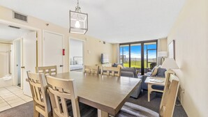 A dining area with a wooden table and chairs, a hanging light fixture, and a view of the outdoors through large windows.