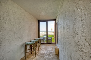 Ein schmaler Korridor mit strukturierter Wandgestaltung, eine Schiebetür zu einem Außenbereich mit Blick auf eine grüne Landschaft und eine Palme.