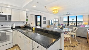 Una cocina moderna con armarios blancos, encimera de granito y vistas a la playa.