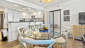 Una cocina moderna con armarios blancos, una mesa de comedor de vidrio y una mesita auxiliar de mimbre.