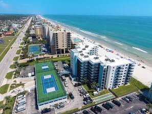 A beachfront hotel with multiple floors, a tennis court, and a parking lot. - Ground Floor Beachfront 2BR with Direct Pool and Car Free Beach Access (New Smyrna Beach)