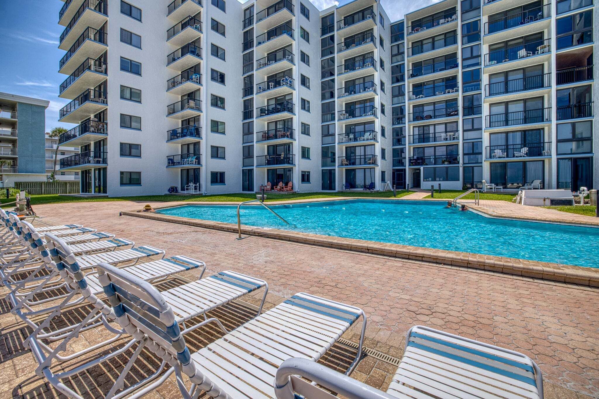 Um edifício de apartamentos moderno com piscina e espreguiçadeiras.