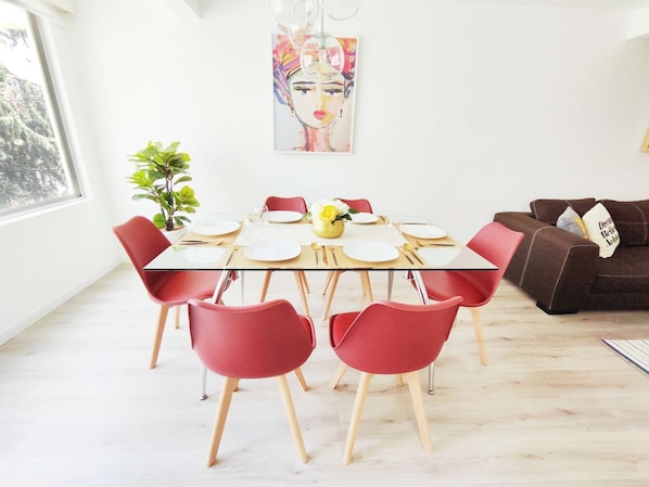 A dining area with a glass table, red chairs, and a modern painting on the wall.
