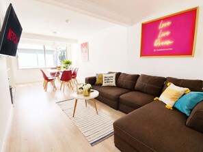 Un salon moderne avec un canapé marron, un téléviseur, un coin repas avec des chaises rouges et une affiche motivante.