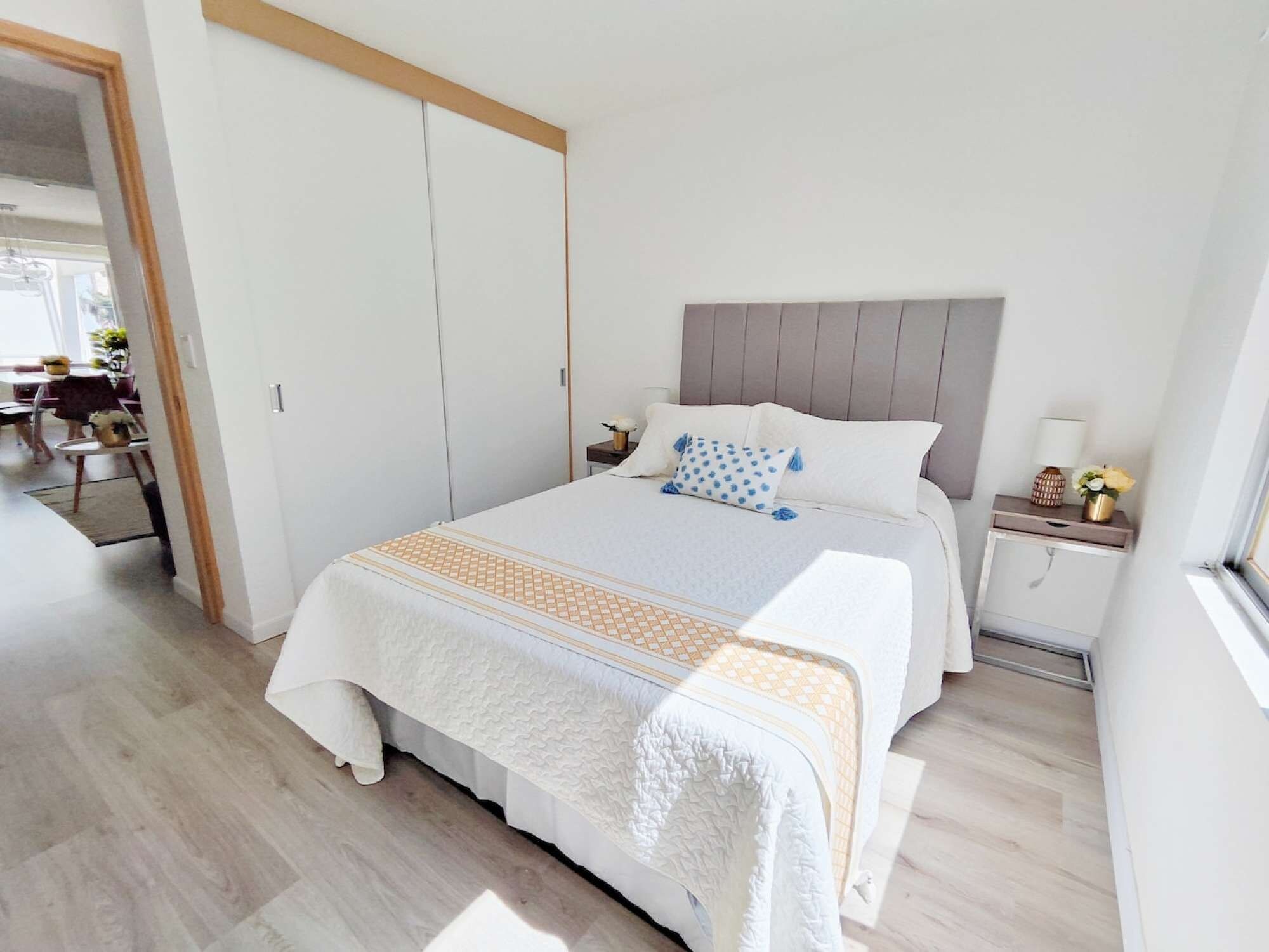 A bedroom with a bed, bedside tables, a nightstand, a window, and a door leading to another room.