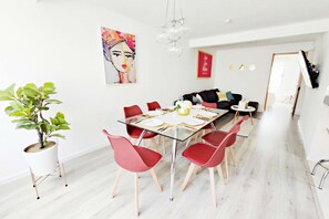 Un espace repas moderne avec une table en verre, des chaises rouges, une plante en pot et un tableau coloré accroché au mur.
