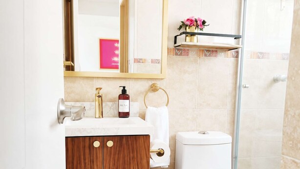 Un baño con tocador de madera, inodoro, cubo de basura y zona de ducha.
