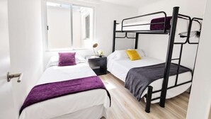 Un dormitorio con dos camas individuales, una ventana, una mesita de noche y una cama litera.