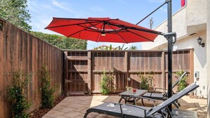Eine Terrasse mit zwei Liegestühlen, einem roten Sonnenschirm und einem Holenzaun.
