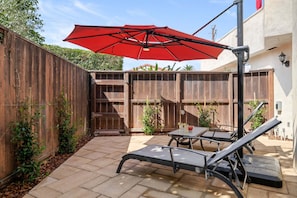 Un patio con dos sillones de descanso, un paraguas rojo y una valla de madera.
