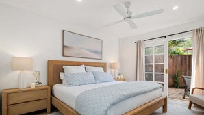 Ein Schlafzimmer mit Bett, Nachttischen, Deckenventilator, Fenster und Blick ins Freie.