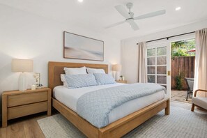 Un dormitorio con cama, mesitas de noche, ventilador de techo, ventana y vista al exterior.