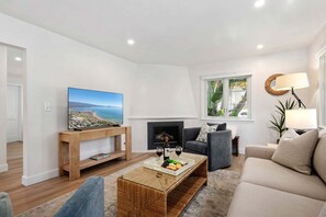 A modern living room with a flat-screen TV, a fireplace, a sofa, and a coffee table with snacks.