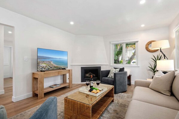 A modern living room with a flat-screen TV, a fireplace, a sofa, and a coffee table with snacks.
