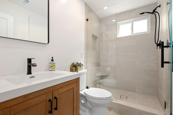 Un baño moderno con un lavamanos blanco, un inodoro y una zona de ducha con paredes de vidrio.