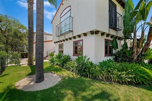 A two-story building with a balcony, surrounded by lush greenery and palm trees.