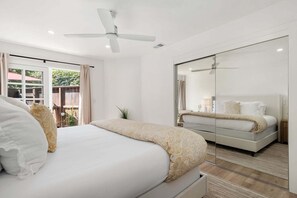 A modern bedroom with a large bed, a bedside table, a mirror, and a ceiling fan.