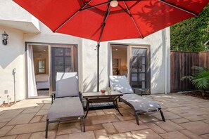 An outdoor patio with two lounge chairs and a red umbrella.