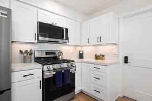 Cocina compacta con muebles blancos, estufa de acero inoxidable, microondas y cafetera.