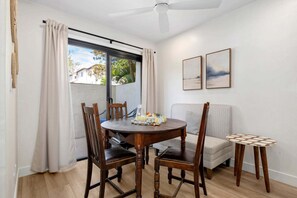 A dining area with a round wooden table, four chairs, a small side table, and a ceiling fan.