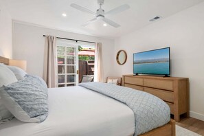 A bedroom with a bed, a television, a ceiling fan, and a view of the outdoors through a glass door.