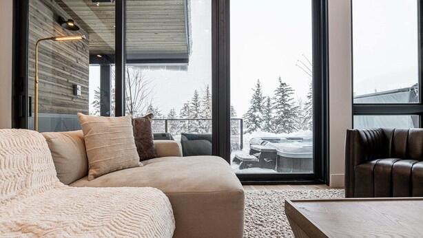 Ein modernes Wohnzimmer mit einer Couch, einem Couchtisch und Blick auf eine verschneite Landschaft durch große Fenster.