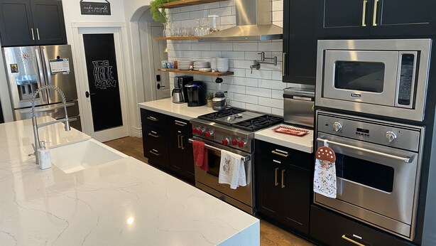 Et moderne køkken med rustfrie stål apparater, mørke skabe og en marmor bordplade.