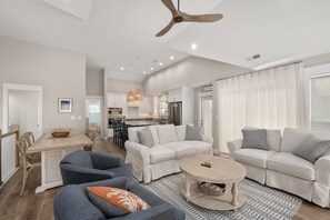 A spacious living room with a dining area, a kitchen in the background, and a ceiling fan. - Shelly Shores - Hot tub, community pool & tennis courts, great views (Nags Head)