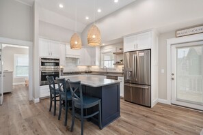 A modern kitchen with white cabinetry, a stainless steel refrigerator, and a central island with bar stools.