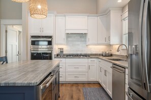 A modern kitchen with white cabinetry, stainless steel appliances, and a granite countertop. - Shelly Shores - Hot tub, community pool & tennis courts, great views (Nags Head)