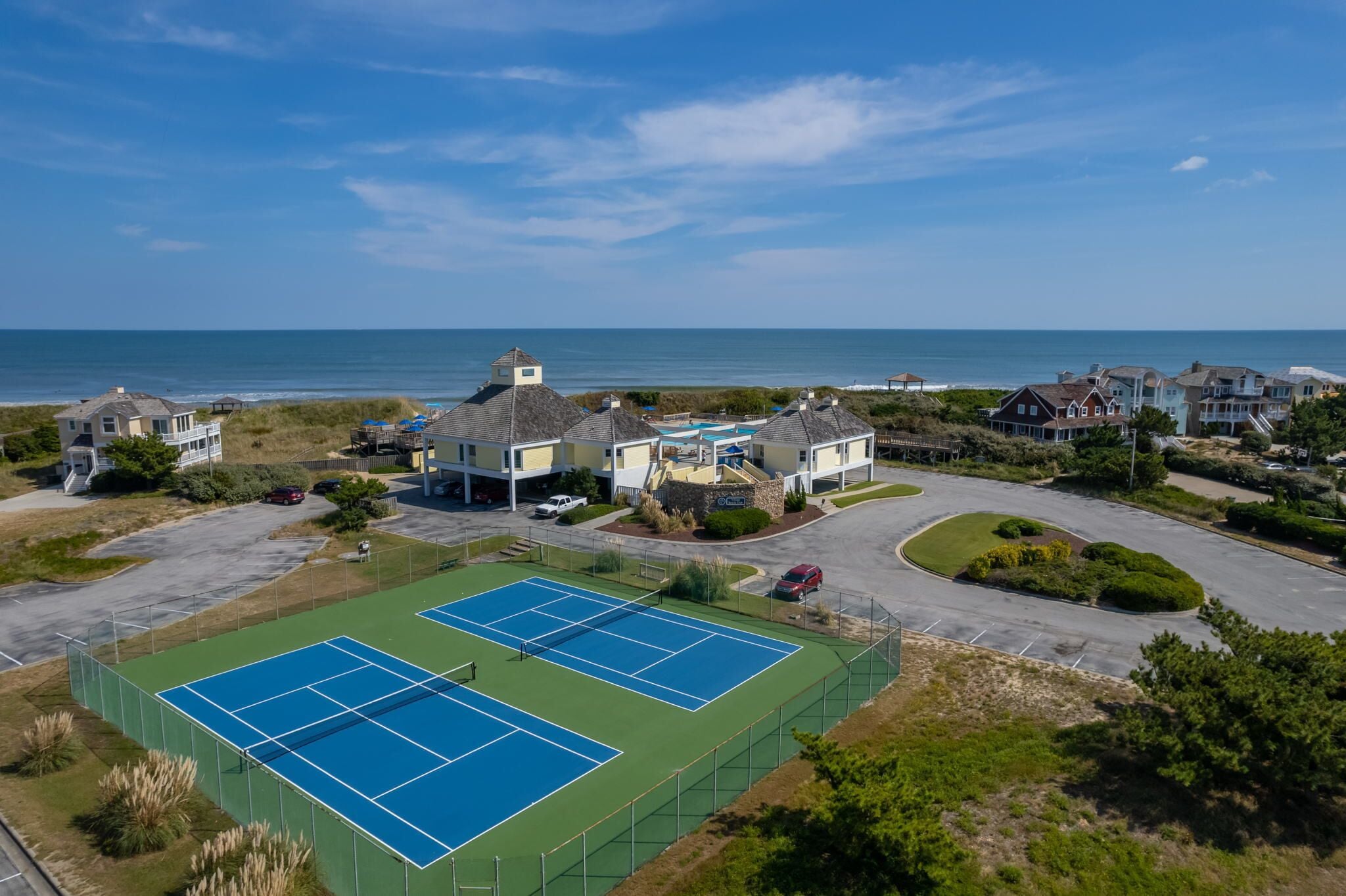 A residential area with two tennis courts, a parking lot, and houses with ocean views.