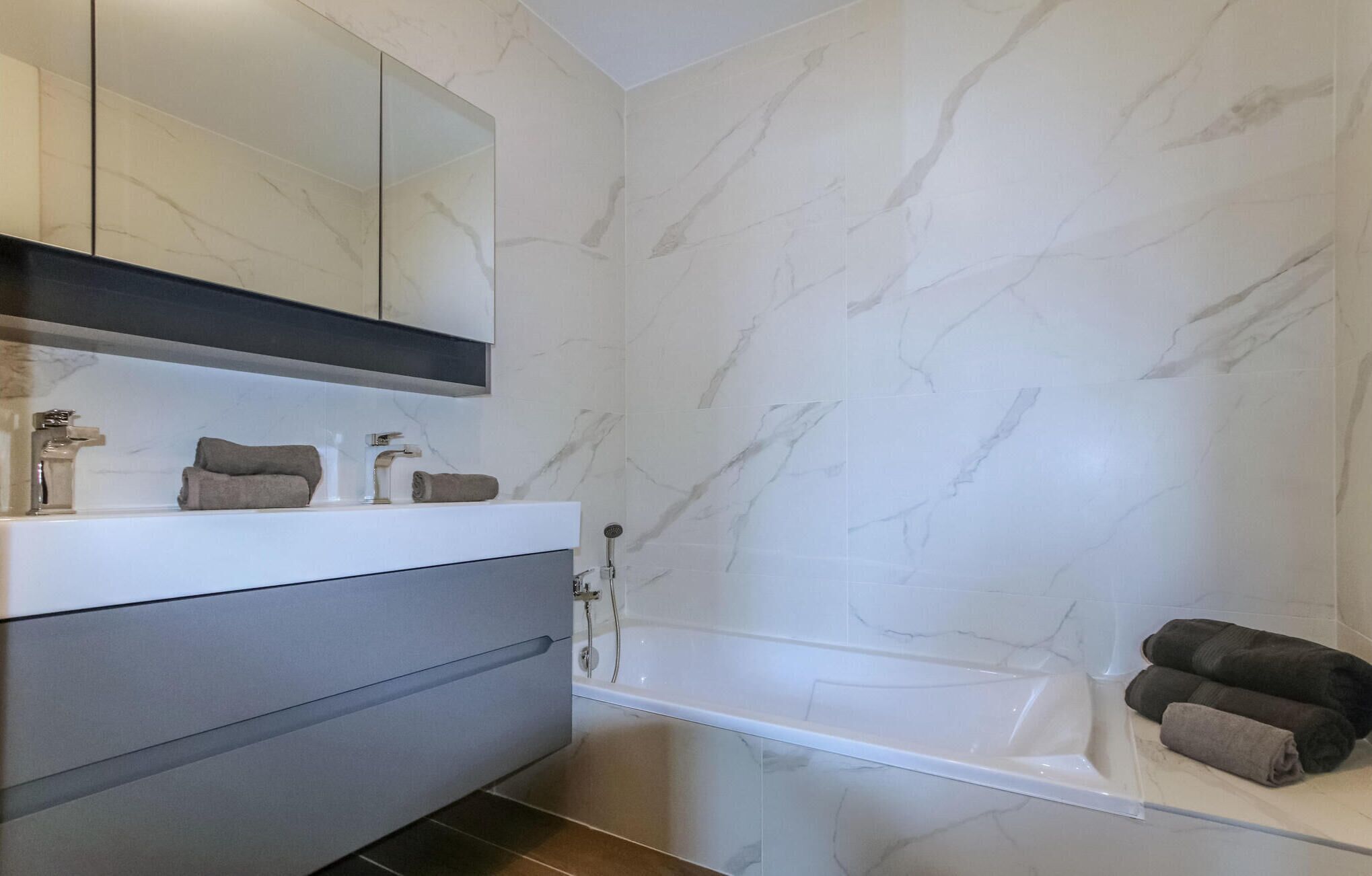 Un baño moderno con pared de mármol, tocador blanco y bañera.