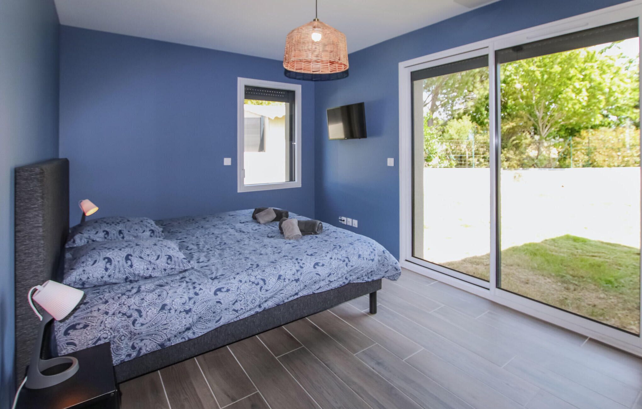 Een slaapkamer met een bed, een bedlamp, een televisie en een grote schuifdeur naar een tuin.