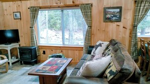 L’intérieur chaleureux d’un chalet avec un canapé, une table recouverte d’une courtepointe, un téléviseur et une cheminée.