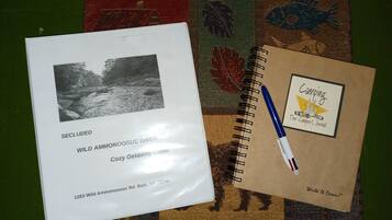 A booklet titled "SECLUDED WILD AMMONOOSUC RIVER COZY GETAWAY CABIN 1283 Wild Ammonoosuc Rd. Bath, NH 03740" and a notebook with a "Camping The Camper's Journal" logo.